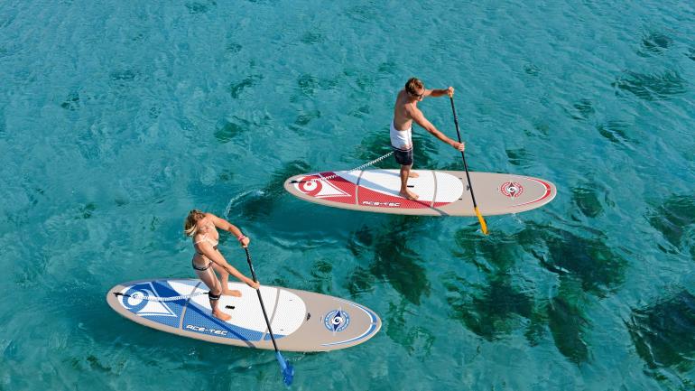 Couple paddleboarding through crystal-clear coastal waters