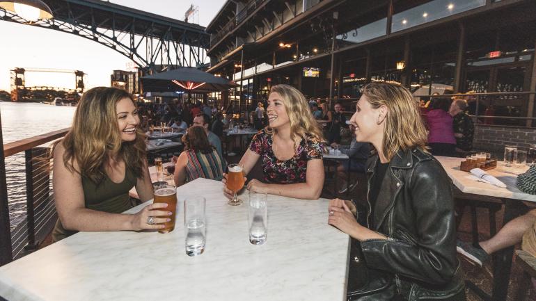 在俄亥俄州克利夫兰的 The Flats 区，一群朋友在水滨享受饮品，悠闲地度过美好时光