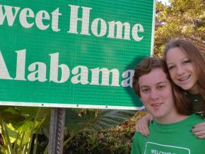 在公路之旅中，站在“阿拉巴马州欢迎您”标志旁拍照留念