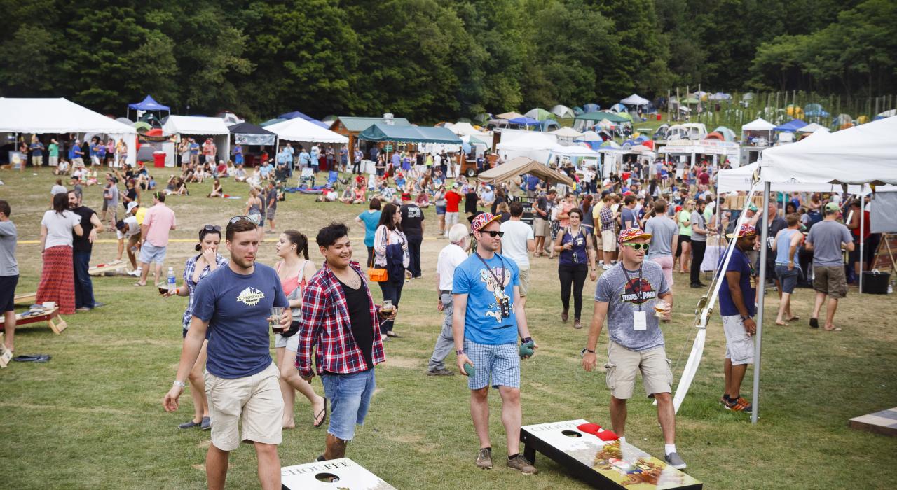 Festival-goers play a game of cornhole with beer in hand 